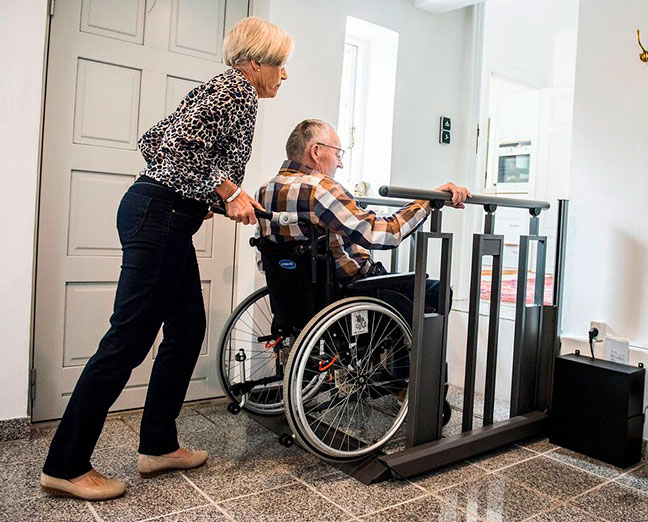 Een vrouw helpt een persoon in een rolstoel met een lift de trap op te gaan